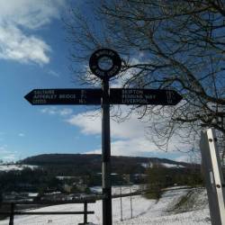 Sign at Bingley Five Rise Locks with field covered in Snow